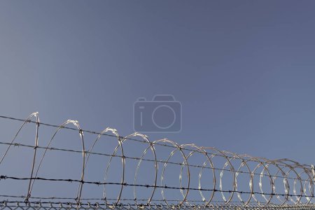 Foto de Muro de prisión de alambre de púas con cerca de alambre de púas cerca perimetral de alambre de afeitar enrollado en el fondo del cielo, alambre de púas. - Imagen libre de derechos
