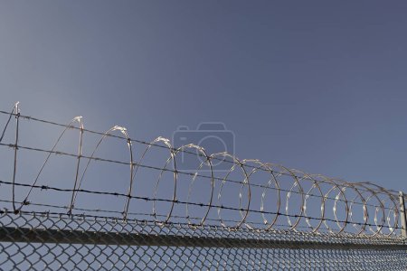 Foto de Muro de prisión de alambre de púas con cerca de alambre de púas cerca perimetral de alambre de afeitar enrollado en el cielo azul, cerca de púas. - Imagen libre de derechos