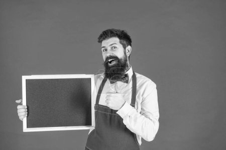 Photo for Happy guy in barber apron give thumbs up approval sign hand gesture holding school blackboard red background copy space, education. - Royalty Free Image