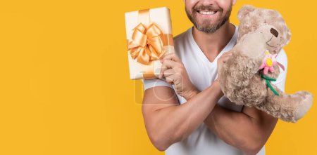 Téléchargez les photos : Photo of man holding valentine present of box and toy, copy space. man hold valentine present isolated on yellow background. man hold valentine present in studio. man with present for valentine day. - en image libre de droit