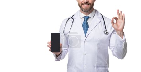 Photo for Medical man crop view. Telehealth doctor holding smartphone showing OK. Medical practitioner. Ehealth. Emedicine. Medical service. Telemedicine, copy space. - Royalty Free Image