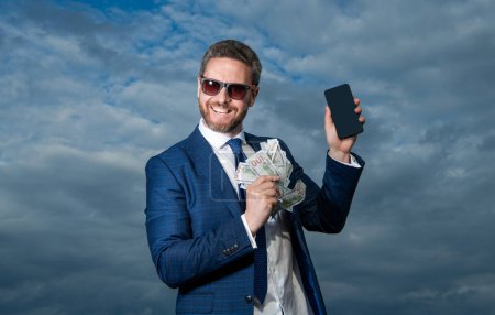 photo of positive betting man with lottery money. betting man with lottery money on sky background. betting man with lottery money outdoor. betting man with lottery money hold phone.