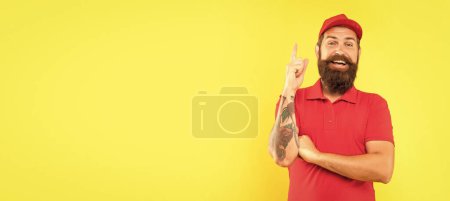 Photo for Happy deliveryman in casual red cap and tshirt keeping finger raised yellow background copy space, idea. - Royalty Free Image