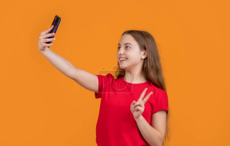 Téléchargez les photos : Heureux enfant faire selfie sur smartphone sur fond jaune. - en image libre de droit