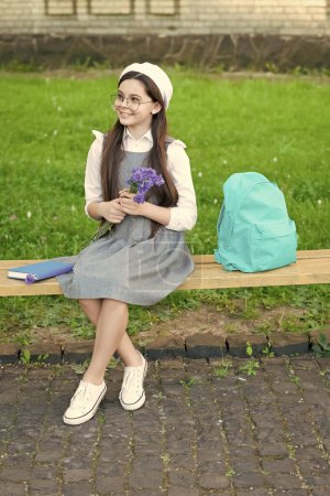 Téléchargez les photos : Enfant heureux dans des lunettes se détendre sur le banc du parc avec des fleurs. 8 mars. - en image libre de droit