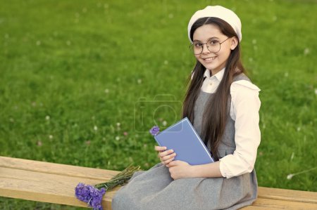 Téléchargez les photos : Enfant heureux dans des lunettes se détendre sur le banc du parc avec livre. espace de copie. - en image libre de droit