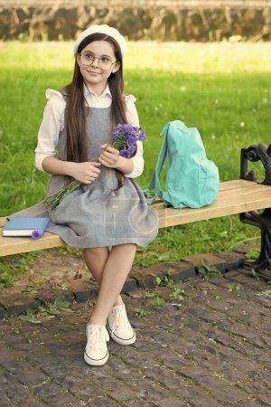 Téléchargez les photos : Enfant heureux dans des lunettes se détendre sur le banc du parc avec des fleurs. Journée des femmes. - en image libre de droit