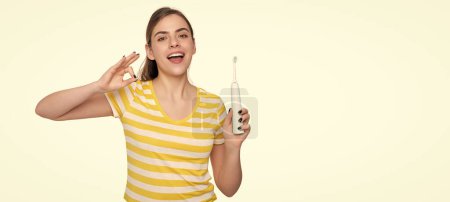 Téléchargez les photos : Joyeuse jeune femme avec brosse à dents électrique isolé sur fond blanc. OK.. - en image libre de droit