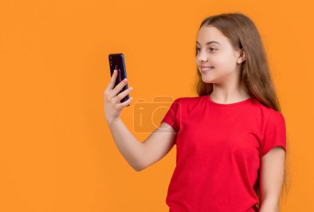 Téléchargez les photos : Enfant gai avec smartphone sur fond jaune. - en image libre de droit