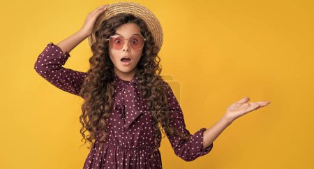 Photo for Amazed child in straw hat and sunglasses with long brunette curly hair presenting product. - Royalty Free Image