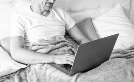 Téléchargez les photos : Mature man in glasses working on laptop in bed. modern life. - en image libre de droit
