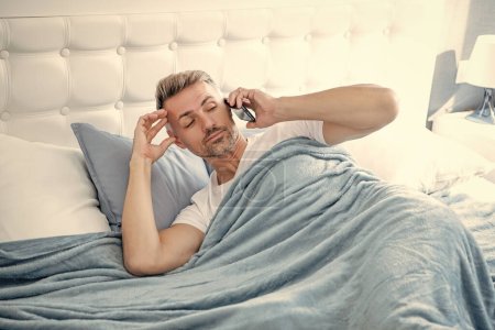 sleepy mature man in bed speaking on phone.