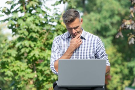 Téléchargez les photos : Réfléchissant homme travaillant sur ordinateur portable. homme pigiste en plein air. homme d'affaires avec PC. - en image libre de droit