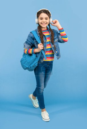 Happy teen girl listening to music in headphones blue background, education. School education. Non-formal education.