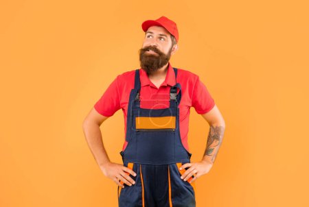 Foto de Thinking bearded man loader in work clothes on yellow background. - Imagen libre de derechos