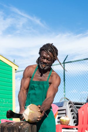 Photo for Nassau, Bahamas - January 07, 2016: pitchman man with dreadlocks cut coconut. - Royalty Free Image