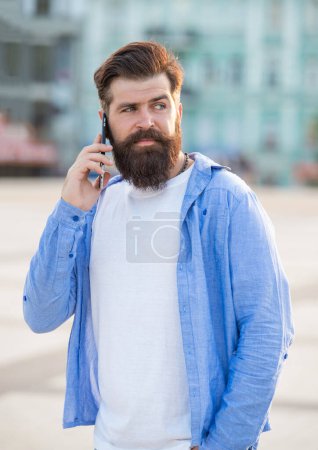 Photo of guy speak on smartphone, answerphone. guy speak on smartphone outdoor. guy speak on smartphone outside. guy speak on smartphone in the street.