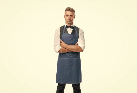 Foto de Confident man in apron and bow keeping arms crossed isolated on white, waiter. - Imagen libre de derechos
