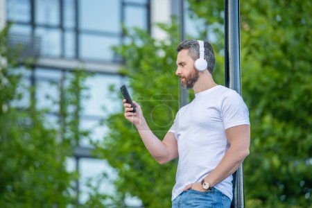 Man choose music playlist in the street, banner. man choosing music playlist outside. photo of man choose music playlist on phone. man choose music playlist outdoor.