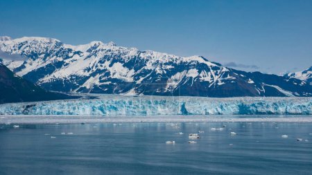 Mountain glacier calving and ice in sea ocean water under blue sky nature. Hubbard Glacier nature in Alaska, USA. Glacier bay nature. Snowy mountain peaks natural landscape and seascape.
