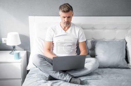 Téléchargez les photos : Mature man using computer in bed with coffee. - en image libre de droit