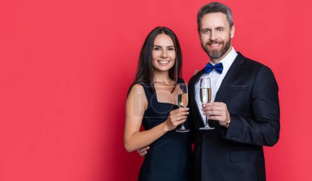 Paar jubelt und feiert im Hintergrund, Werbung. Foto des Paares beim Jubeln und Feiern mit Champagner. Paar jubelt und feiert isoliert auf Rot. Paar jubelt und feiert