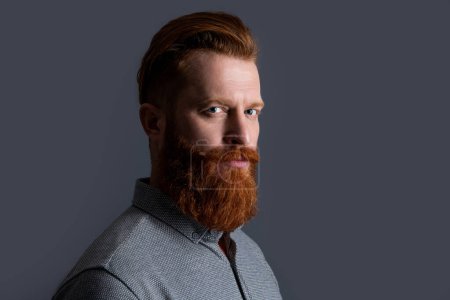Retrato del hombre irlandés con la cara sin afeitar medio turno. Un hombre serio con barba roja y bigote. Estudio hombre barbudo aislado en gris, espacio de copia.
