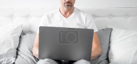 Téléchargez les photos : Mature homme travaillant sur ordinateur portable au lit. - en image libre de droit