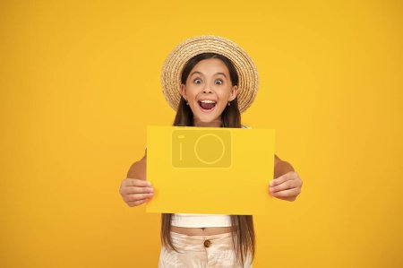 Photo for Surprised teen girl hold empty advertisement paper with copy space on yellow background. - Royalty Free Image