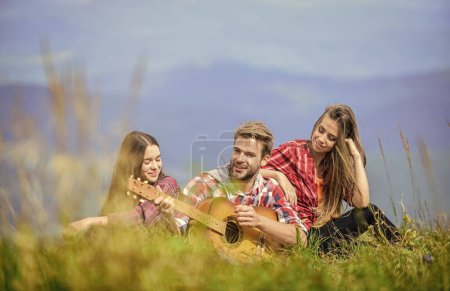 Photo for People relaxing on mountain top while handsome man playing guitar. Singing together. Musical pause. Hiking entertainment. Peaceful place. Melody of nature. Hiking tradition. Friends hiking with music. - Royalty Free Image