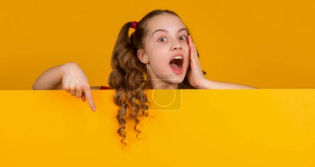 Photo for Amazed child behind blank yellow paper with copy space for advertisement. point finger. - Royalty Free Image