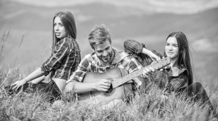 Photo for Friends hiking with music. Nothing but friends and guitar. People relaxing on mountain top while handsome man playing guitar. Hiking entertainment. Peaceful place. Melody of nature. Hiking tradition. - Royalty Free Image