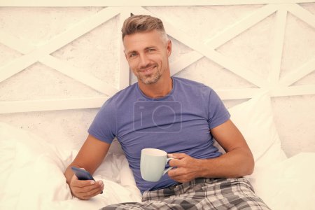 photo of happy man messaging in morning at home. man messaging in morning. man messaging in morning in bed. man messaging in morning in bedroom.