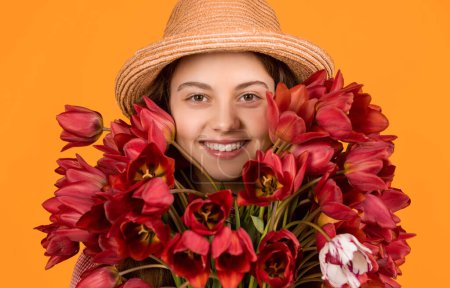 Smiling child in hat hold spring tulip flowers on yellow background.