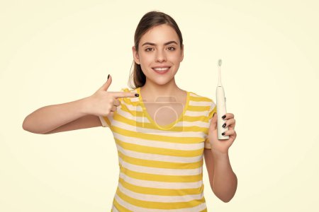 Téléchargez les photos : Joyeuse jeune femme pointe du doigt sur brosse à dents électrique isolé sur fond blanc. - en image libre de droit