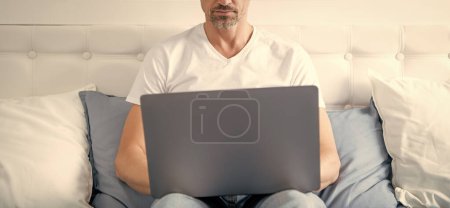 Téléchargez les photos : Mature homme travaillant sur ordinateur portable au lit. - en image libre de droit