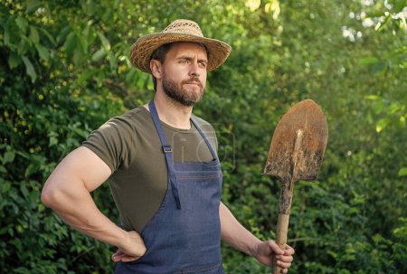 Photo for Thoughtful farmer man in farmers hat and gardening apron holding garden shovel natural outdoors. - Royalty Free Image