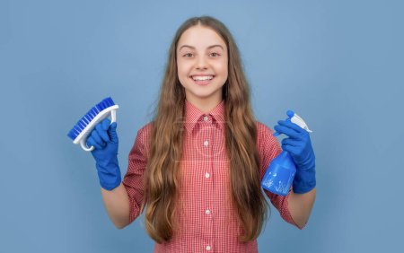 happy child in rubber gloves with spray bottle and brush on blue background.