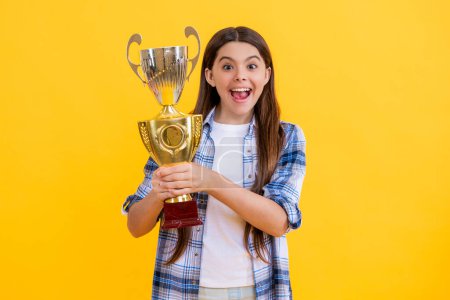 shocked teen girl accept award on background. proud teen girl with champion cup award. teen girl hold her award champion cup isolated on yellow. teen girl receive award in studio.