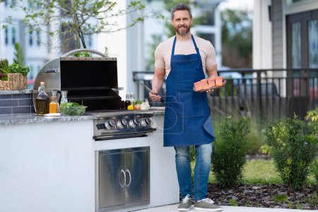 full length of chef man cooking salmon on grill outdoor. grill salmon fish at man wear apron. photo of man with grill salmon. man cook salmon on grill.