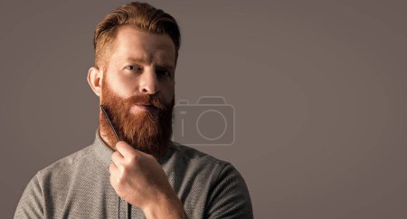 Photo for Bearded man combing beard isolated on grey background with copy space. man with beard combing hair. man has beard in studio. man combing beard with haircomb. combing and styling. - Royalty Free Image