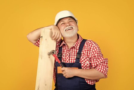 positive old aged man woodworker in helmet on yellow background.