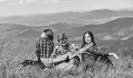 Photo for Hiking tradition. Friends hiking with music. Nothing but friends and guitar. People relaxing on mountain top while handsome man playing guitar. Hiking entertainment. Peaceful place. Melody of nature. - Royalty Free Image