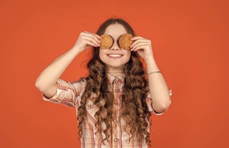 Glad teen girl with oatmeal cookies on orange background.