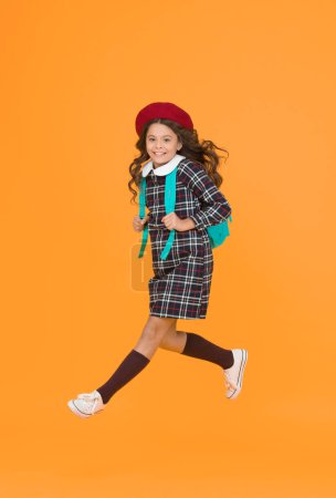 Photo for Stylish teen college student jumping. little girl with backpack going to school. education concept. school and fashion. child in pupil uniform. kid in french beret on yellow background. hurry up. - Royalty Free Image