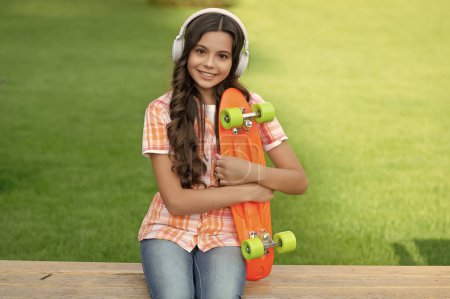 Photo for Glad teen girl with skateboard outdoor. teen girl with skateboard in headphones. teen girl with skateboard outside. photo of teen girl with skateboard listen music. - Royalty Free Image
