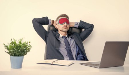 Müder Unternehmer entspannt sich in Schlafmaske am Arbeitsplatz.