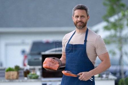 Photo for Man cook salmon in apron, banner. photo of man cook salmon food. man cook salmon on grill. man cook salmon outdoor. - Royalty Free Image