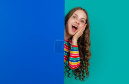 Foto de Impactado adolescente niño detrás de blanco papel azul con espacio de copia para la publicidad. - Imagen libre de derechos