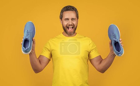 surprised fitness man with sneakers in studio. photo of fitness man with sneakers shoes. fitness man with sneakers isolated on yellow. fitness man with sneakers on background.